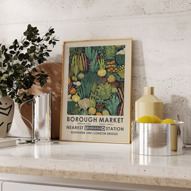 Puede incluir: Un p&oacute;ster enmarcado con un borde dorado que presenta una colorida ilustraci&oacute;n de varias verduras. El p&oacute;ster dice "BOROUGH MARKET" con informaci&oacute;n sobre la estaci&oacute;n de metro m&aacute;s cercana. La obra de arte est&aacute; sobre un fondo neutro.