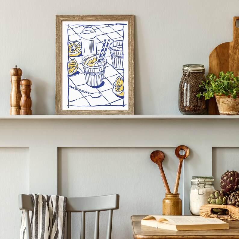 Pu&ograve; includere: Una stampa incorniciata con un'illustrazione blu e gialla di una bevanda rinfrescante con limoni, una bottiglia e un bicchiere. La stampa &egrave; esposta su una mensola con utensili da cucina in legno, un barattolo di grani di pepe e una piccola pianta in vaso.