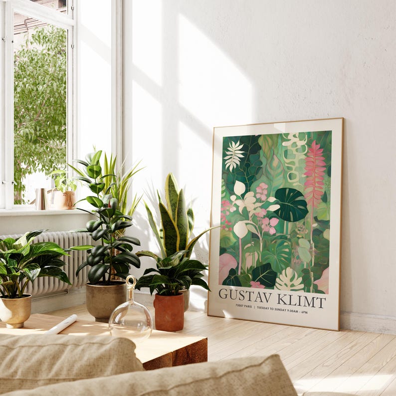 May include: A framed art print featuring a vibrant botanical illustration in shades of green, pink, and white. The print is propped against a white wall, surrounded by potted plants. The text "GUSTAV KLIMT" is visible.