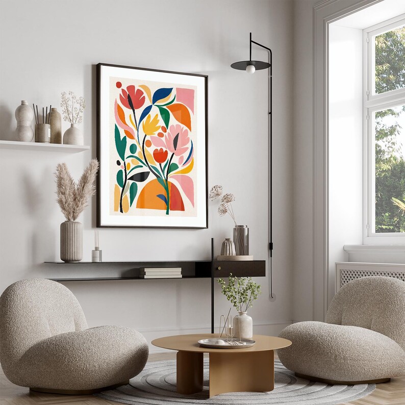 May include: A framed floral art print with a black border. The artwork features abstract flowers in shades of pink, orange, yellow, and blue against a cream background. The print is displayed in a modern living room setting.