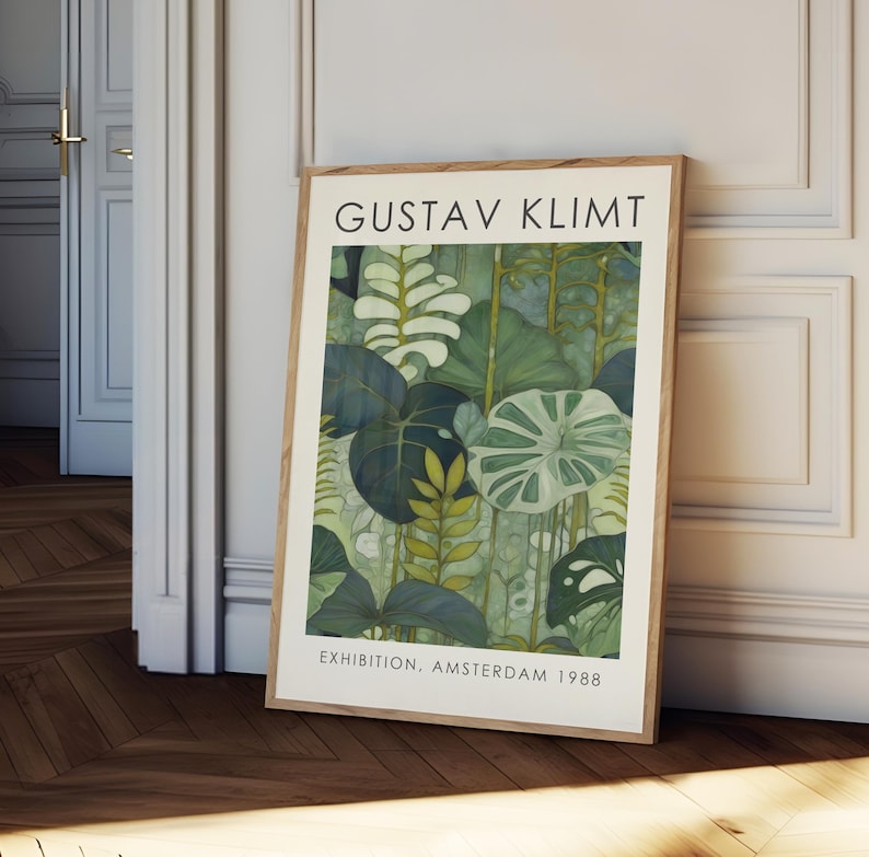 May include: A framed art print featuring a botanical illustration in shades of green and blue. The print is titled "GUSTAV KLIMT" and includes the text "EXHIBITION, AMSTERDAM 1988". The artwork is displayed in a light-colored wooden frame.