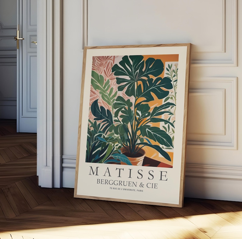 Puede incluir: Un grabado art&iacute;stico enmarcado con una ilustraci&oacute;n bot&aacute;nica de varias plantas verdes en una maceta de terracota. La obra de arte tiene un fondo beige con el texto "MATISSE BERGGRUEN & CIE" y la direcci&oacute;n "70 RUE DE L'UNIVERSITE, PARIS". El marco es de madera marr&oacute;n claro.