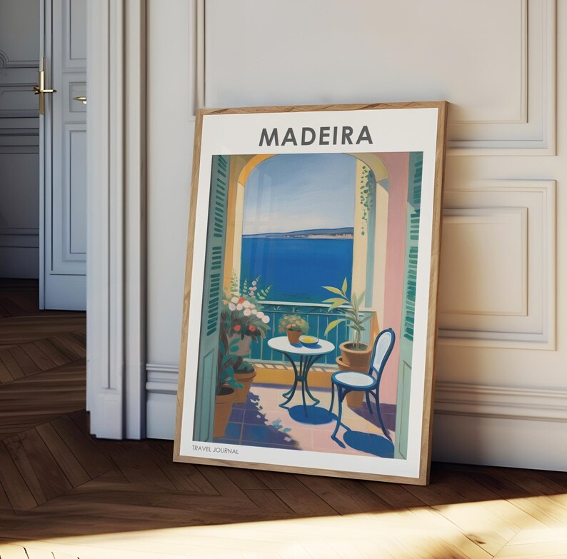 May include: A framed poster with a colorful illustration of a balcony overlooking the ocean. The poster has the word "MADEIRA" in white text at the top and "TRAVEL JOURNAL" in white text at the bottom.