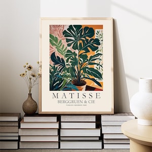 Puede incluir: Una impresi&oacute;n art&iacute;stica enmarcada con una ilustraci&oacute;n bot&aacute;nica de una planta en maceta con grandes hojas verdes. La impresi&oacute;n incluye el texto "MATISSE BERGGRUEN & CIE" y se exhibe sobre una pila de libros, con un jarr&oacute;n de flores secas y un jarr&oacute;n blanco cerca.