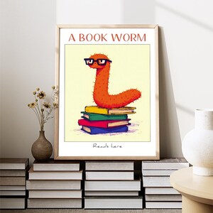 May include: A bookworm with glasses sits on top of a stack of colorful books. The text "A BOOK WORM" is at the top of the image and "Reads here" is at the bottom.