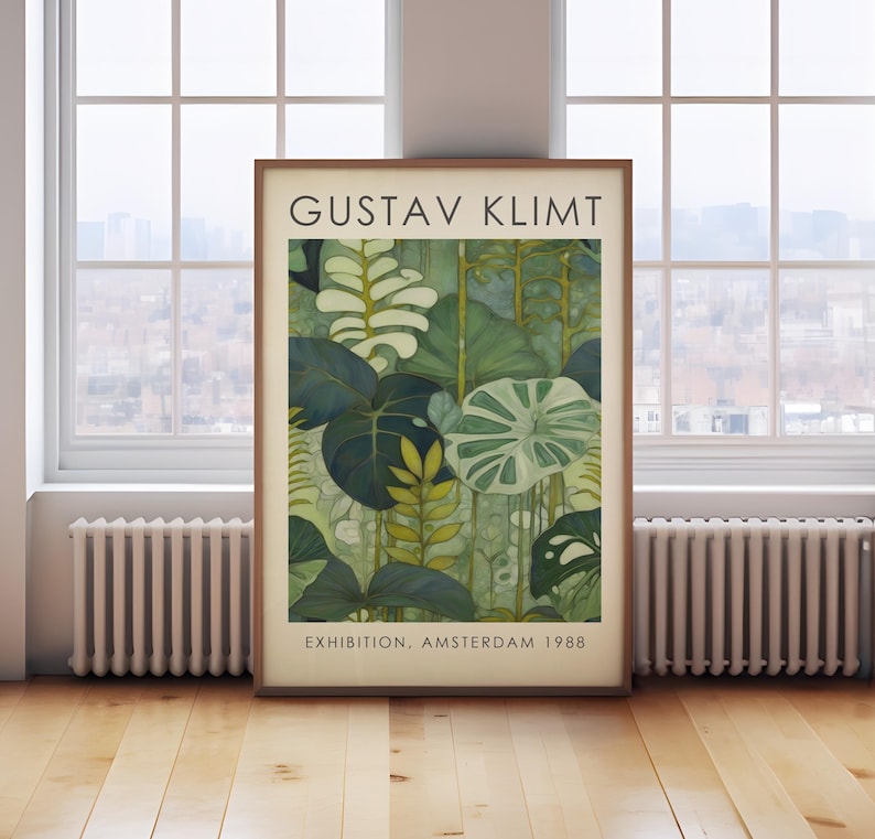 May include: A framed art print featuring a botanical illustration in shades of green and white. The print is labeled "GUSTAV KLIMT" and "EXHIBITION. AMSTERDAM 1988". The artwork is displayed on a wooden floor near a window.