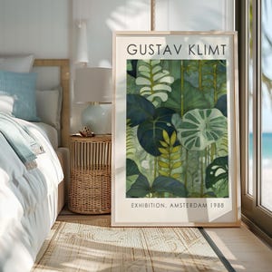 May include: A framed art print featuring a botanical illustration in shades of green, with the text "GUSTAV KLIMT" at the top and "EXHIBITION, AMSTERDAM 1988" at the bottom. The artwork is displayed in a bright room with a bed and a side table.