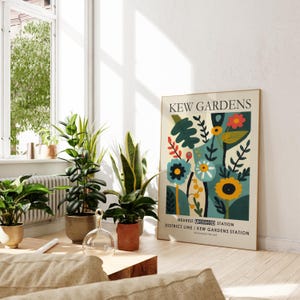 May include: A framed poster with the text "KEW GARDENS" and a colorful floral design. The poster is propped against a wall near several potted plants. The room is bright with natural light.