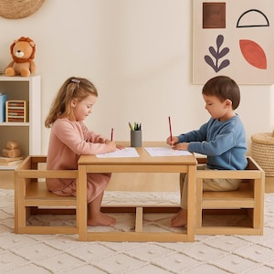 May include: A light wood children's table and chair set. Two children are seated at the table, each drawing with a red pencil on a white sheet of paper. A stuffed lion toy sits on a shelf in the background.