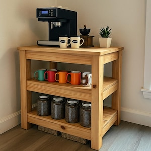 May include: A wooden coffee station with a black espresso machine, coffee grinder, and small potted plant. The shelves hold colorful mugs and glass jars filled with coffee beans. The station is made of light-colored wood.
