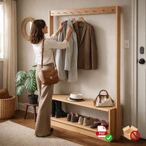 May include: A wooden entryway organizer with a coat rack, shoe storage, and a bench. A woman is hanging a light gray coat on the rack. A brown blazer hangs next to it. A white purse and a hat sit on the bench.