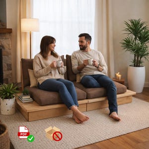 以下が含まれることがあります： 茶色のクッションが付いた明るい木製のプラットフォームソファ。カップルがソファに座り、それぞれ白いマグカップを持っています。ソファは、フロアランプ、鉢植えの植物、ニュートラルカラーのラグのあるリビングルームにあります。