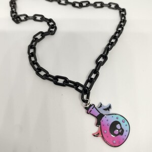 May include: A black chain necklace featuring a colourful glass potion bottle pendant. The bottle has a skull design and a pink, blue and purple ombre effect.