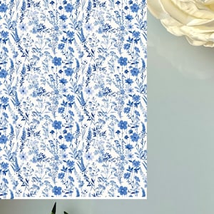 May include: A close-up of a white background with a blue floral pattern. The pattern features various flowers and foliage in shades of blue. A white rose is in the upper right corner. The image is of a floral design.