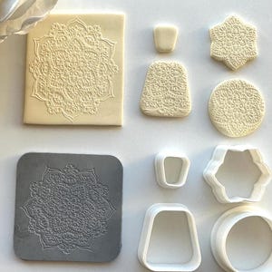 May include: A selection of cookie cutters and embossed biscuits. The biscuits are in various shapes, including square, hexagonal, and circular, all featuring a detailed floral mandala design. The cutters are white and grey.