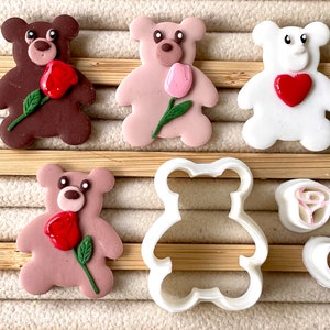 May include: Four brown, pink and white teddy bear clay charms with a rose or tulip flower and a heart. A white plastic teddy bear cookie cutter is also included.