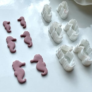May include: A set of white plastic seahorse cookie cutters and six pink fondant seahorse shapes.