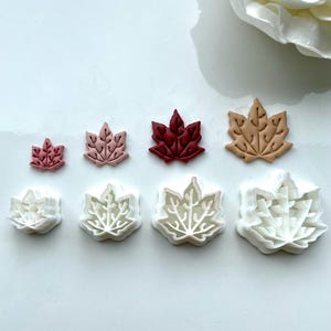 May include: Set of six leaf-shaped cookie cutters in various sizes. The cutters are made of white plastic and are arranged in a row on a white surface. The cutters are in different sizes, with the smallest cutter on the left and the largest cutter on the right.