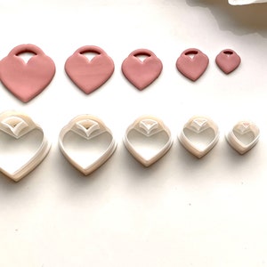 May include: Set of six heart-shaped cookie cutters in various sizes. The cutters are made of white plastic and have a smooth finish. The cutters are arranged in two rows, with the largest cutter at the top and the smallest cutter at the bottom.