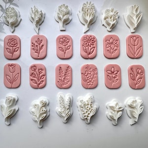 May include: A collection of white plastic floral cookie cutters and their corresponding pink clay impressions. The set includes various botanical designs such as roses, tulips, and wildflowers, arranged in rows to display the stamp and cutter shapes.