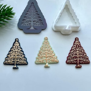 May include: A selection of Christmas tree-shaped moulds and decorations. The moulds are in dark grey and white, while the decorations are in navy blue, light green, and burgundy, with gold accents. The designs feature intricate patterns.
