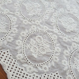 Broderie anglaise vintage lace in a light cream white with a rose motif laid out on a vintage wooden table, close up detail.