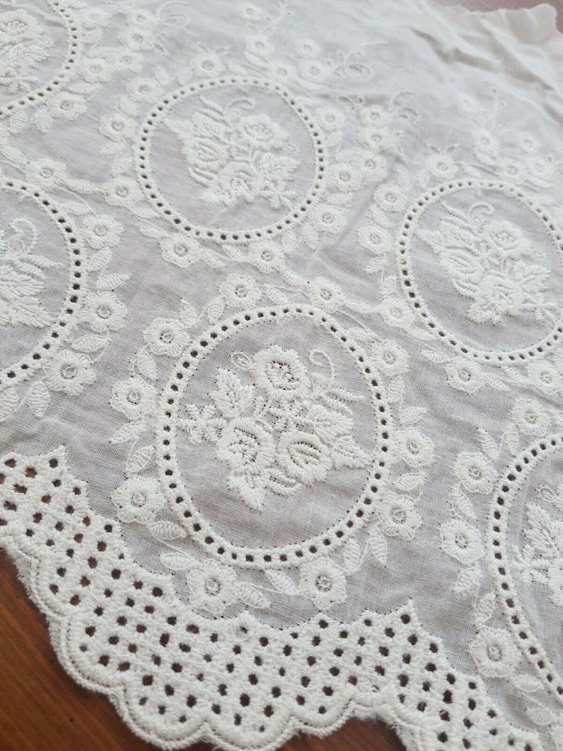 Broderie anglaise vintage lace in a light cream white with a rose motif laid out on a vintage wooden table, close up detail.