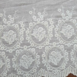 Broderie anglaise vintage lace in a light cream white with a rose motif laid out on a vintage wooden table, clear view of a whole section.