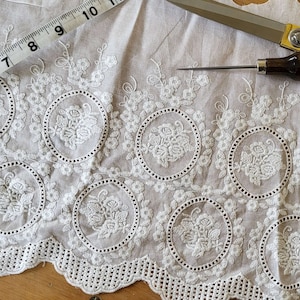 Broderie anglaise vintage lace in a light cream white with a rose motif laid out on a vintage wooden table surrounded by vintage sewing tools
