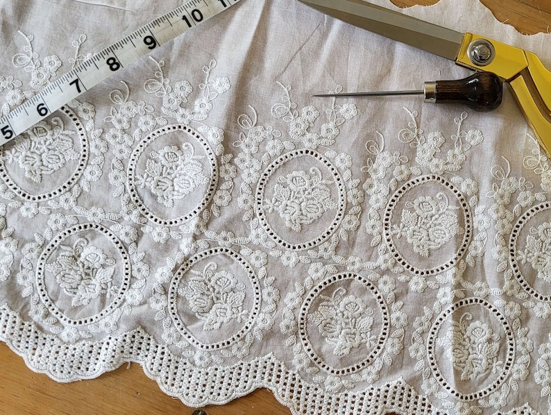 Broderie anglaise vintage lace in a light cream white with a rose motif laid out on a vintage wooden table surrounded by vintage sewing tools