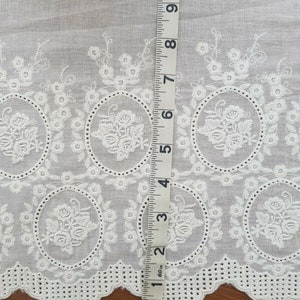 Broderie anglaise vintage lace in a light cream white with a rose motif laid out on a vintage wooden table with a tape measure laid out on it for size reference
