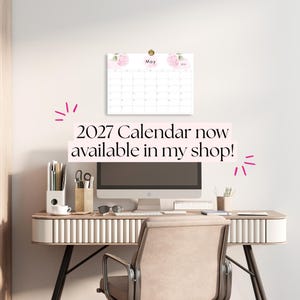 K&ouml;nnte beinhalten: Ein Wandkalender f&uuml;r 2027 mit einem Blumendesign und rosa Hortensien-Illustrationen am oberen Rand. Der Kalender zeigt den Monat Mai und ist &uuml;ber einem Computermonitor an der Wand befestigt, auf einem Schreibtisch mit B&uuml;robedarf.