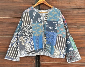 Può includere: Una giacca in patchwork blu e bianca con scollo a V e maniche lunghe. La giacca è in cotone e ha un design trapuntato.