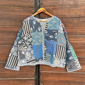 Peut inclure: Une veste en patchwork bleu et blanc avec un col en V et des manches longues. La veste est en coton et a un design matelassé.