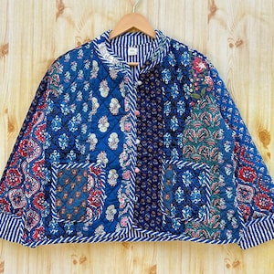 Könnte beinhalten: Eine blaue gesteppte Jacke mit Patchwork-Design, das Blumen- und Paisley-Muster zeigt. Die Jacke hat einen Stehkragen, einen Knopfverschluss und zwei Taschen.