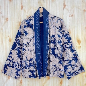 Peut inclure: Une veste matelassée bleu marine avec un imprimé floral beige. La veste a un col châle et des manches longues.