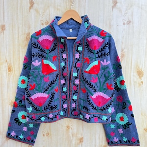 May include: A blue cropped jacket with long sleeves and floral embroidery in shades of pink, red, green, and black.