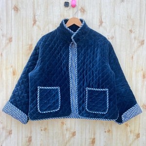 May include: A dark blue quilted jacket with a white and blue striped lining. The jacket has a stand-up collar, a zip closure, and two patch pockets.