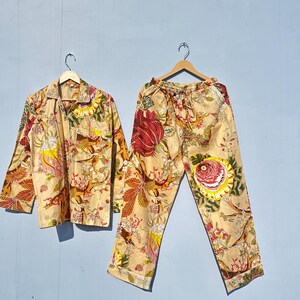 May include: A beige pajama set with a floral print featuring red, yellow, and green flowers. The set includes a long-sleeved shirt and pants.