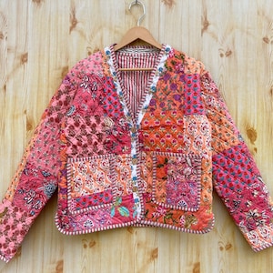 Può includere: Una giacca trapuntata patchwork rosa e arancione con scollo a V e chiusura con bottoni. La giacca ha due tasche e una stampa floreale.