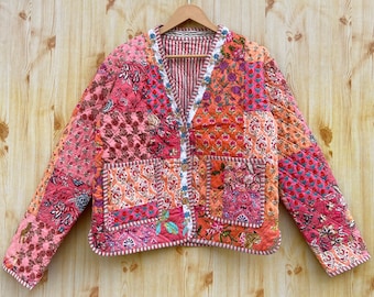 May include: A pink and orange patchwork quilted jacket with a V-neck and button closure. The jacket has two pockets and a floral print.