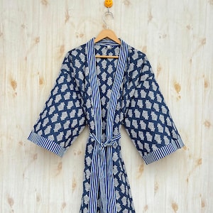 Op de afbeelding: Een blauw en wit badjas met patroon en bijpassende riem. De badjas heeft een ruitvormig bloemmotief en gestreepte accenten op de kraag, mouwen en riem. De badjas hangt aan een houten kleerhanger.