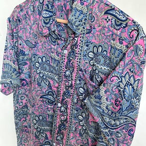Op de afbeelding: Een overhemd met knopen en een levendig paisley-patroon in roze, blauw en grijs. Het overhemd heeft een klassieke kraag en manchetten met knopen. De stof ziet er zacht en vloeiend uit.