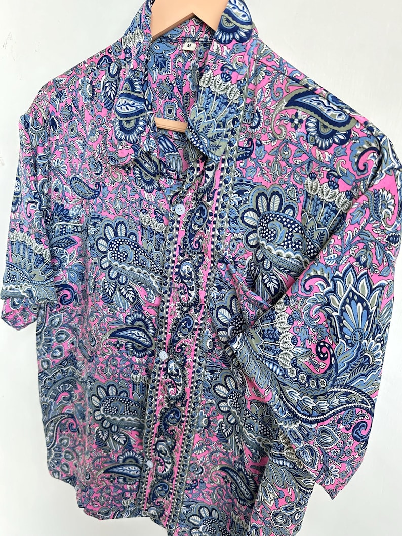 Op de afbeelding: Een overhemd met knopen en een levendig paisley-patroon in roze, blauw en grijs. Het overhemd heeft een klassieke kraag en manchetten met knopen. De stof ziet er zacht en vloeiend uit.
