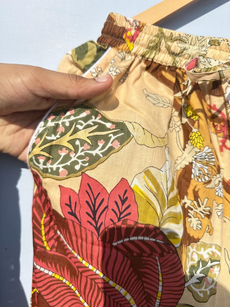 Op de afbeelding: Beige pyjamabroek met een bloemenprint met rode, groene en gele bladeren. De broek heeft een witte elastische tailleband en een trekkoord.
