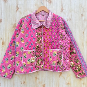 May include: A pink quilted jacket with a floral print and a button-up closure. The jacket has two pockets and a contrasting trim.