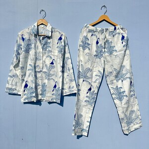May include: A white pyjama set with a blue and white tropical print featuring toucans and palm trees. The set includes a long-sleeved shirt with a button-up front and matching trousers with an elastic waistband.