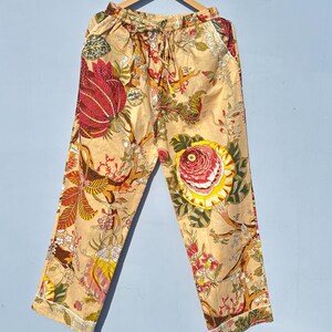 Op de afbeelding: Beige broek met een bloemenprint met rode, gele en groene bloemen. De broek heeft een elastische tailleband en een trekkoord.