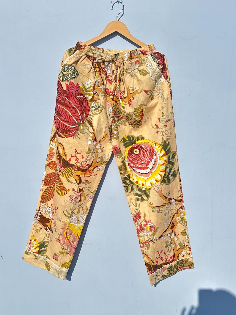 Op de afbeelding: Beige broek met een bloemenprint met rode, gele en groene bloemen. De broek heeft een elastische tailleband en een trekkoord.