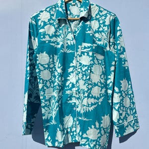 Pu&ograve; includere: Una camicia a maniche lunghe blu turchese con una stampa floreale bianca. La camicia ha una chiusura con bottoni sul davanti e una tasca sul petto sinistro.